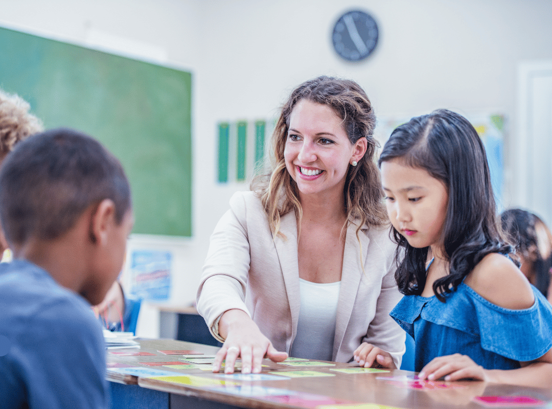 Smiling teacher sitting with students pointing at something on the table