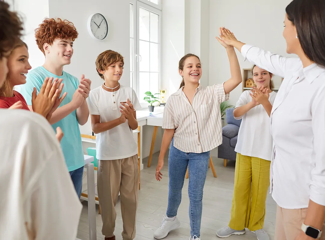 Room full of kids and a teacher standing in a circle with one student giving a high five