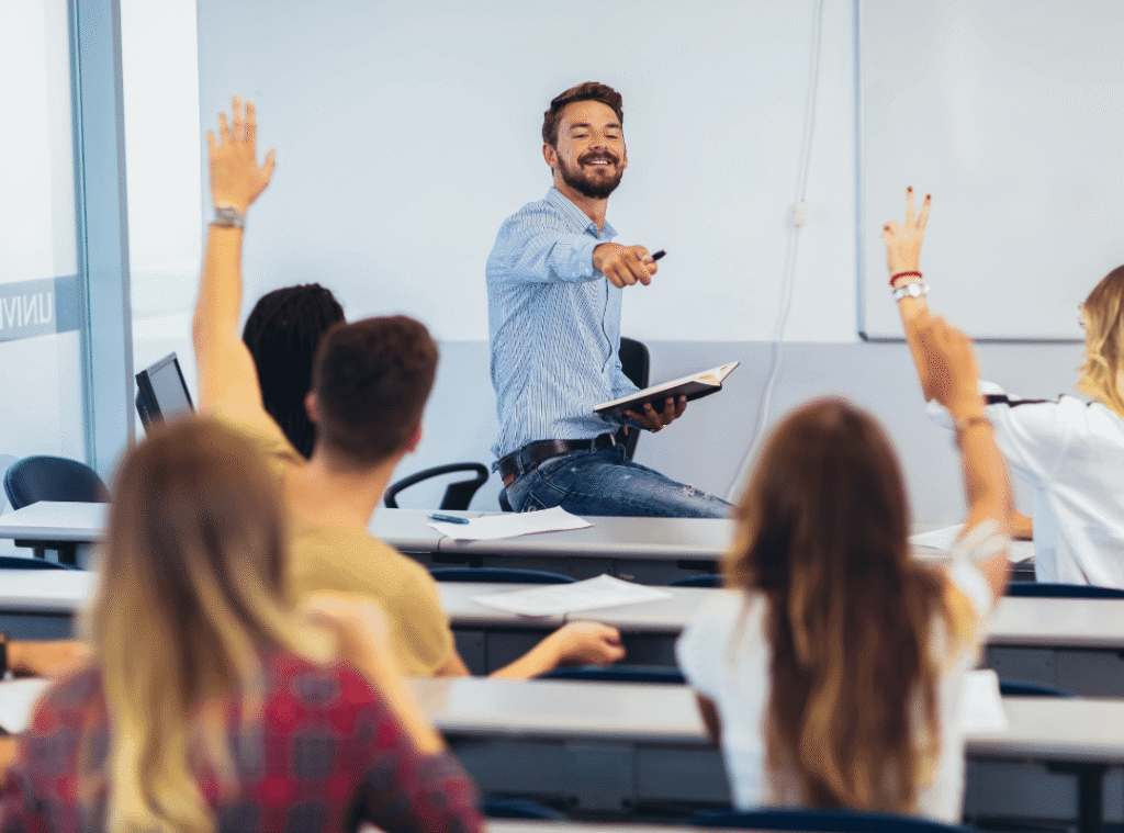 Classroom with adults, male teacher pointing at student with their arm raised.